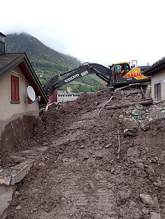 STRABAG-Bagger räumt Schlammmassen zwischen zwei Häusern. 