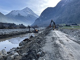 Bild mit zwei Baggern an der Reuss und Bergen im Hintergrund