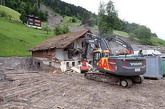 STRABAG-Bagger räumt Schlammmassen zwischen zwei Häusern. 