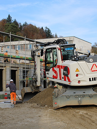 Arbeiten bei der Baustelle im November 2024, Bagger im Vordergrund hinten Rohbau