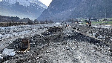 Bild mit zwei Baggern an der Reuss und Bergen im Hintergrund